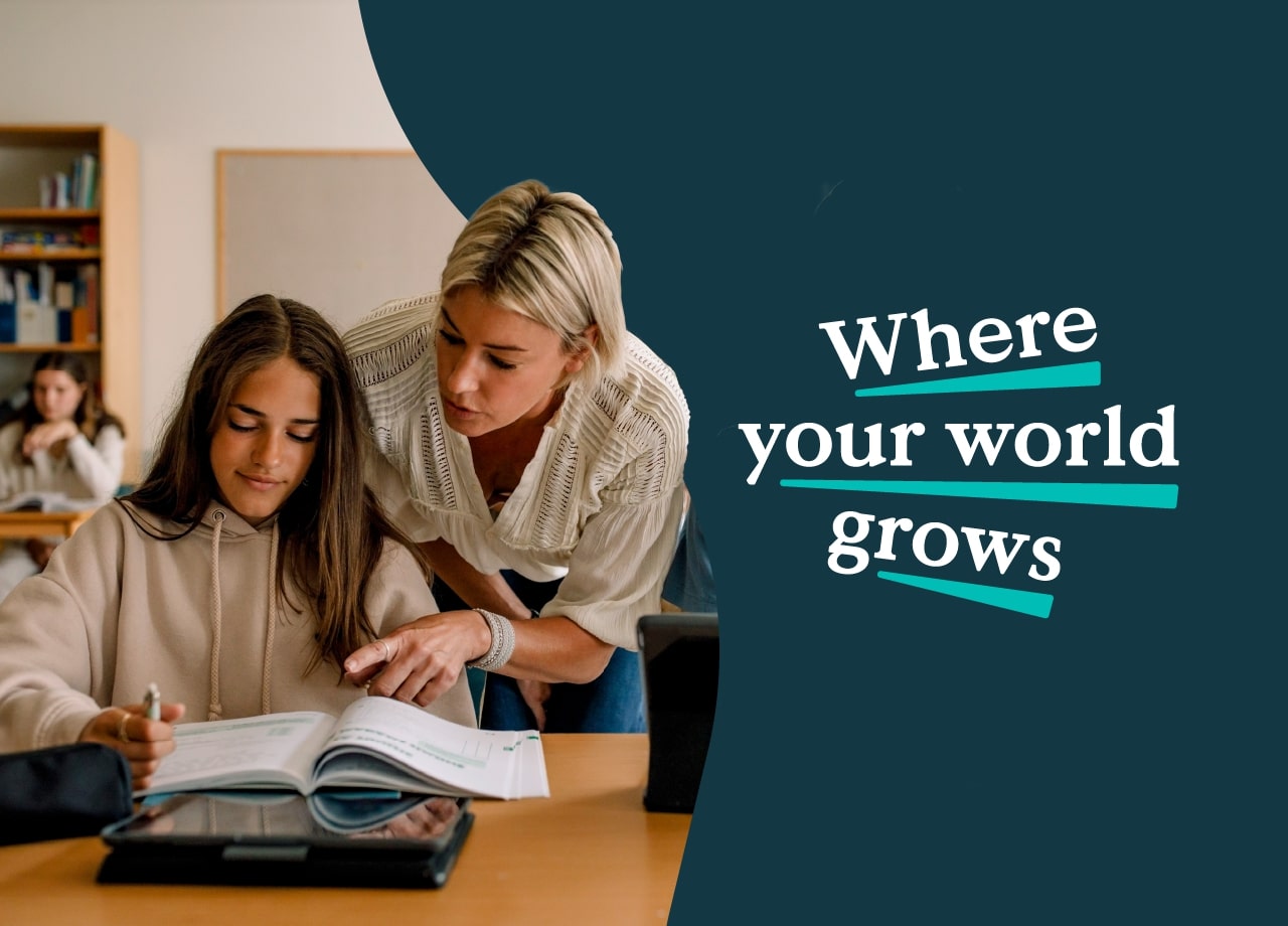 Teacher helping student in classroom with books and tablet.
